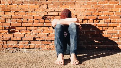 bullied young boy in hat sadly leaning against a wall